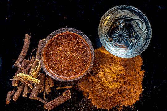 Close up of raw revand chini along with its powder and some lukewarm water with it on a black wooden surface.