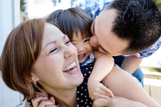Happy little Asian girl carried by her mom and kissed by her dad