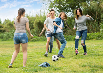 Group of happy teenagers playing football together on green lawn in park .