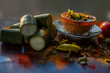 Close up shot of Gujarati famous Galka Nu Shaak on a glass plate. Shot of sponge gourd dish in a glass plate along with all the spices on a brown with some fresh tomatoes and sponge gourd.