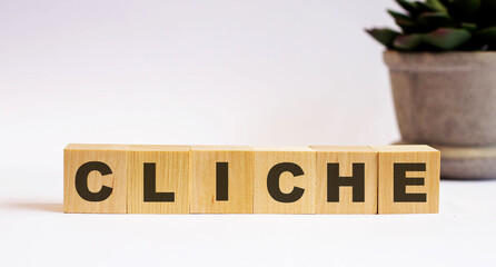 The word CLICHE is written on wooden cubes on a light background near a flower in a pot