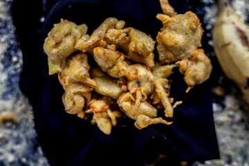 The famous shot of banana bhajia in a black colored container along with some raw banana and spices that are needed to make it. - obrazy, fototapety, plakaty