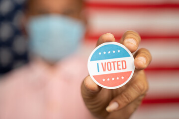 Close up shot man in medical mask showing I voted Sticker and putting on shirt with US flag as...