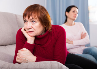 Unhappy women sitting at sofa after conflict at home interior.