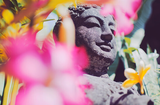 Stone carved statue of Buddha surrounded with colorful flowers