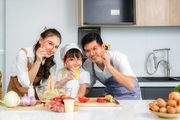Asian family with father, mother and cute little girl daughter  in chef's hats are having fun while cooking in kitchen at home.