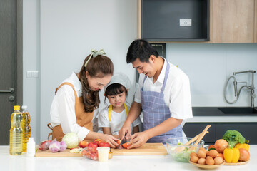 Young Asian love family are preparing salad vegetable on table in the kitchen which father and mother teaching daughter to cooking food on the day at home..
