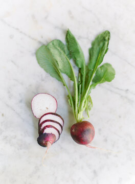 Single organic purple radish with a sliced version on a marble table