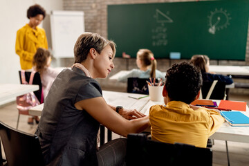 Young teacher assisting to student with learning during a class in the classroom.