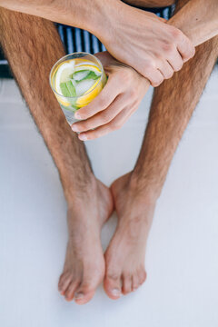 Hands and feet of young man taking a cocktail on a hammock in a pool from above