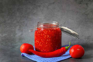 Ground hot red pepper with tomatoes in a glass jar on a dark background. A spicy seasoning made from pepper and tomatoes at home. Home cooking.