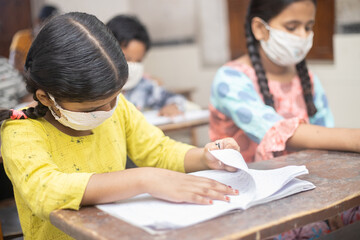 Indian Students wearing face masks sitting with social distancing at a classroom as school reopen during covid19 pandemic. omicron cases