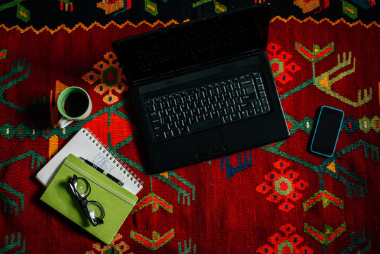 Laptop computer with various objects on the colourful rug