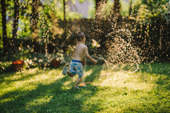 Little boy running through crazy sprinklers in the backyard, intentionally defocused