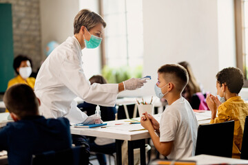Doctor measuring temperature of schoolboy with infrared thermometer in the classroom.