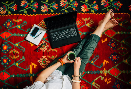 Woman sitting on the floor with laptop and drinking coffee