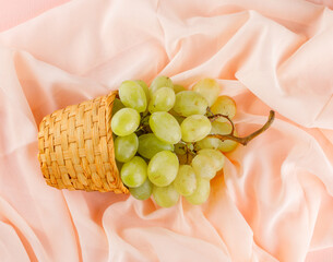 Green grapes in a wicker basket flat lay on a pink textile background