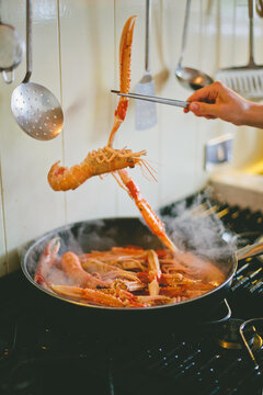 Detail of hand holding picers and lifting a langoustine over steaming pan
