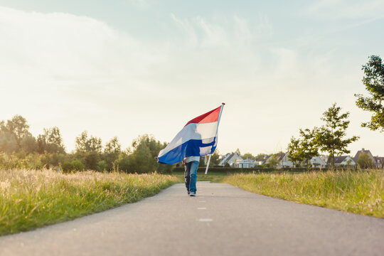 Boy walking a long road holding a Dutch flag in the sunlight