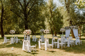 Wedding ceremony outdoors in the park. White chairs decorated with roses.
