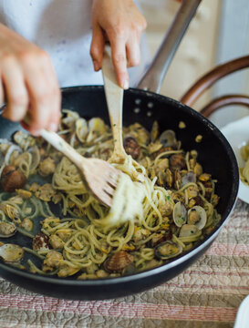Girl mixing spaghetti clams with giant wooden spoon and fork in pan