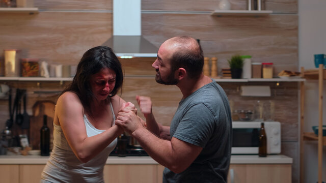 Drunk partner abusing woman in the kitchen. Abused terrified beaten wife covered in bruises suffering injury from alcoholic violent brutal aggressive husband screaming and fighting.