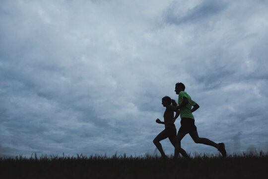 Motivated young couple running together outside on cold, windy night - silhouette