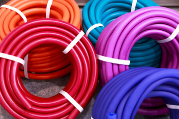 Lots of new multicolored coils of polymer hoses for watering, garden goods and tools in stock on display case for sale