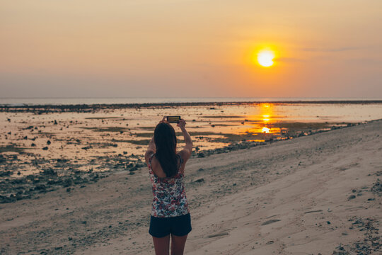 Beautiful young woman taking photos with smartphone on the sunset.