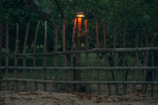 Lamp on a beautiful old fence made by wooden trunks. Night street.