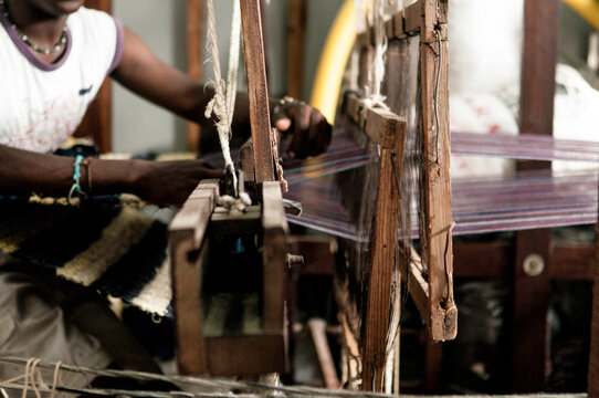 Young African Man uses a loom to make material in workshop