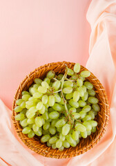 Green grapes in a wicker basket on pink and textile background. top view.