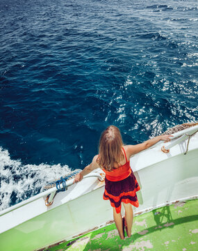 Young woman in sundress sailing on ship looking at sea.