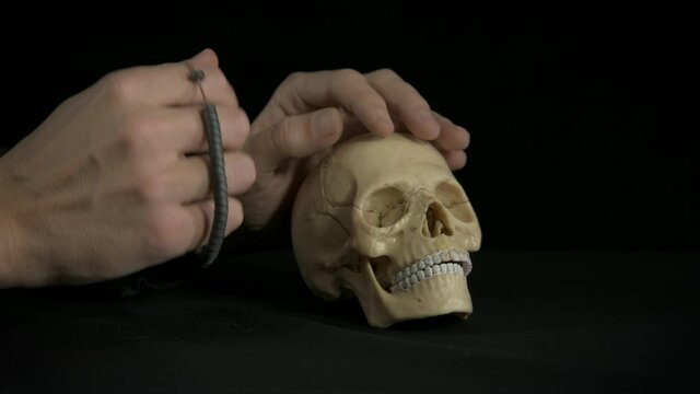 Pray by a skull. A view of a man's hand with a prayer beads by the skull on the black background.