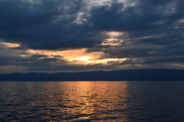evening bright yellow orange sunset with dark blue clouds on lake baikal with a mountain ridge on the horizon
