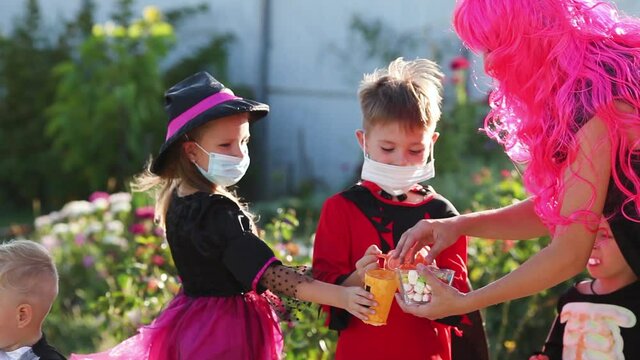 Children trick or treat in Halloween costume and medical mask. A boy and a girl in suits during the coronavirus pandemic receive candy from a woman