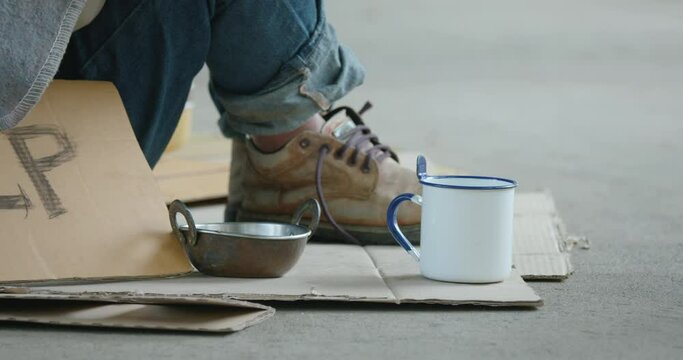 Close up on the cup of homeless man which people giving coin money