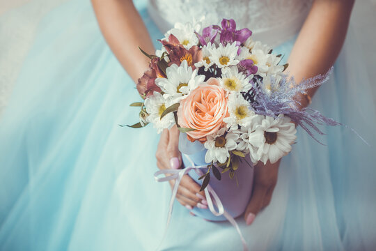Female hands with a box of flowers on the background of a white wedding dress.