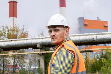 A man in a construction helmet against the backdrop of a large plant.