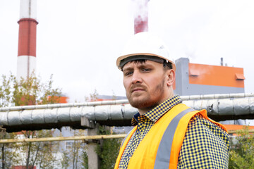 A man in a construction helmet against the backdrop of a large plant.