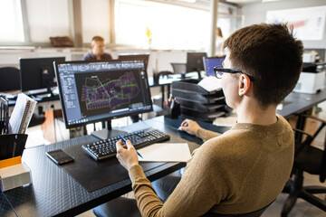 Engineer designer working on desktop computer in factory - obrazy, fototapety, plakaty
