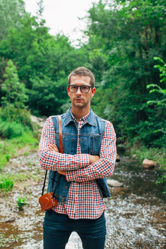 Portrait of a young hipster man with crossed arms. He is holding a vintage photo camera.