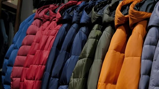 Close up on a raw of mens winter down jackets on a clothes rack in a retail fashion store. Colorful clothing for cold weather. Sale, low price, assortment.