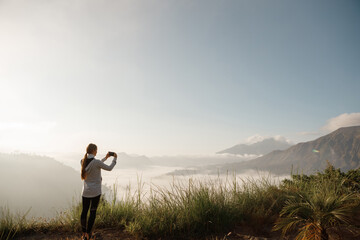 Young cucasian woman backpacker taking photo with smartphone on mountain peak, enjoy sunrise foggy view