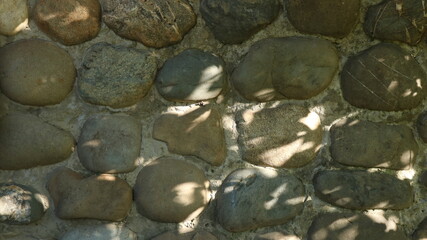rounded large natural stones in the structure of a concrete wall in the design of a rustic fence or...