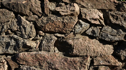 stone dark textured background illuminated by bright sunlight with rough contours of raw natural stone