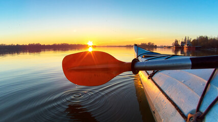Close up shot of person canoeing in the river on a winter sunset. Paddle and blue kayak