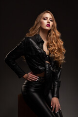 Fototapeta na wymiar Stylish beautiful blonde girl in black leather clothes on a gray background in the studio