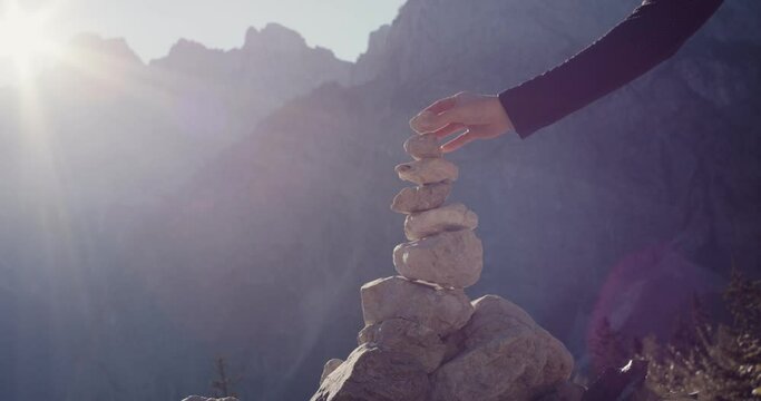 Female hand put stone on stack or cairn zen relaxation meditation balance autumn hiking travel in protected mountain nature in Alps Vr&scaron;ič pass close up slow motion flare beautiful fall light