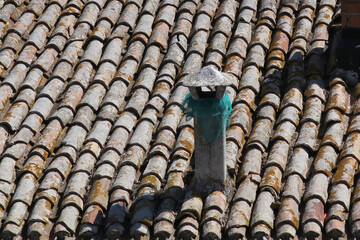 roof with old fashioned rootiles and a chimney covered with green fabric